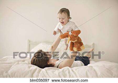 Stock Photo - Caucasian mother playing with baby on bed. Fotosearch
