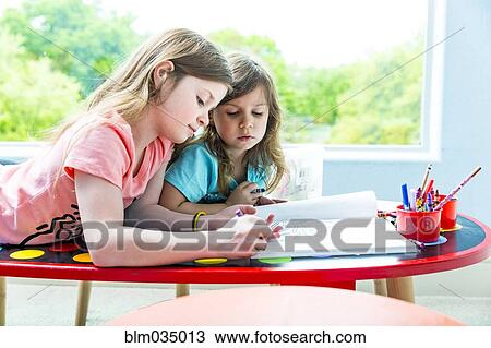 Stock Image - Caucasian sisters drawing at table in playroom. Fotosearch