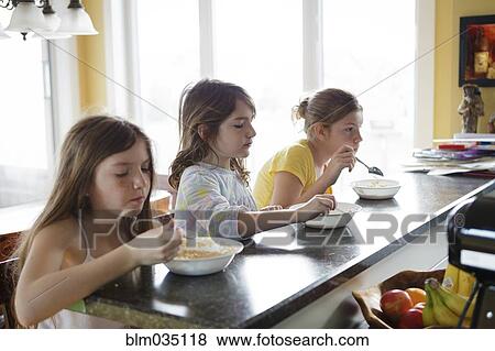 Stock Photo - Caucasian sisters eating breakfast in kitchen. Fotosearch