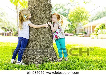 Stock Photo - Caucasian sisters hugging tree in backyard. Fotosearch