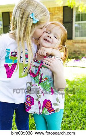 Stock Photo - Caucasian sisters kissing in backyard. Fotosearch