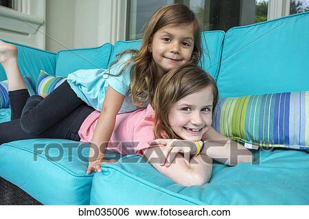 Stock Photograph - Caucasian sisters playing on sofa. Fotosearch