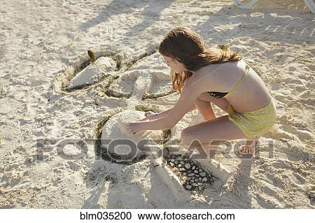 Stock Image - Caucasian teenage girl building sandcastle on beach. Fotosearch