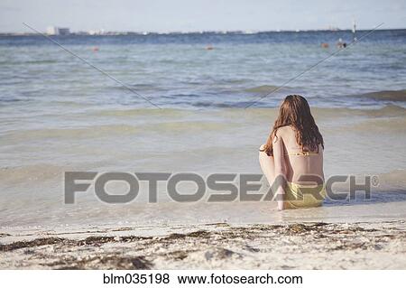 Stock Photo - Caucasian teenage girl sitting in waves on beach. Fotosearch