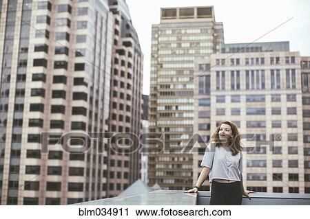Stock Image - Caucasian woman on urban rooftop admiring cityscape. Fotosearch