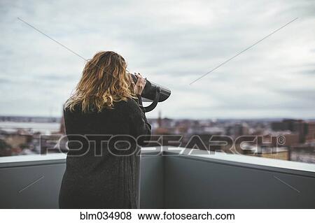 Stock Photo - Caucasian woman on urban rooftop admiring cityscape with telescope. Fotosearch