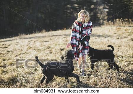 Stock Image - Caucasian woman playing with dogs in rural field. Fotosearch