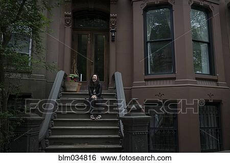 Stock Photograph - Caucasian woman sitting on townhouse front stoop. Fotosearch
