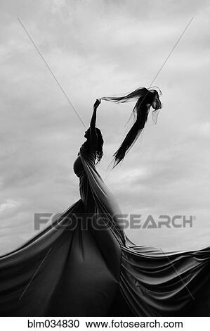 Stock Image - Caucasian woman twirling in fabric under clouds. Fotosearch