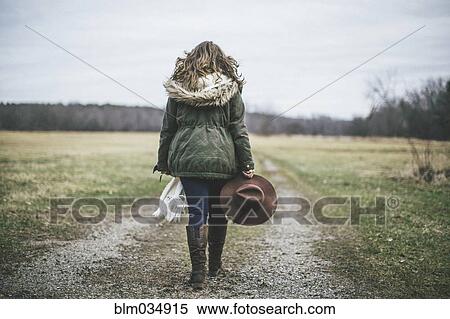 Stock Photography - Caucasian woman walking on dirt path in rural field. Fotosearch