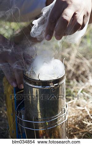 Picture - Close up of beekeeper using smoke for beehive. Fotosearch