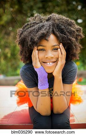 Stock Image - Close up of Black girl sitting on picnic table. Fotosearch