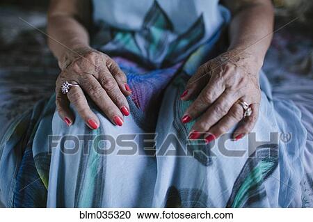 Stock Image - Close up of hands of older woman resting on knees. Fotosearch