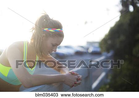 Stock Image - Close up of woman leaning over fence in parking lot. Fotosearch