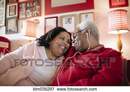 Stock Photo - Couple listening to earbuds in living room. Fotosearch