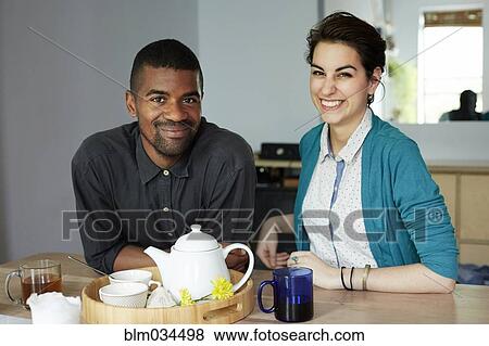 Stock Photo - Couple smiling with tea at table. Fotosearch