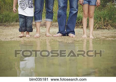 Stock Image - Family wearing jeans at still puddle. Fotosearch