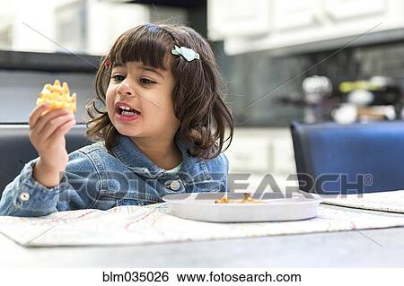 Stock Photograph - Girl eating waffle fries in kitchen. Fotosearch