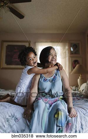 Stock Photo - Grandmother and granddaughter hugging on bed. Fotosearch
