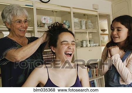 Stock Photo - Grandmother styling hair of granddaughter in dining room. Fotosearch