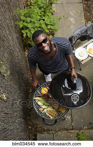 Stock Photography - High angle view of African American man grilling at barbecue. Fotosearch