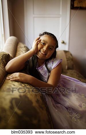 Stock Image - Hispanic girl sitting on sofa in living room. Fotosearch