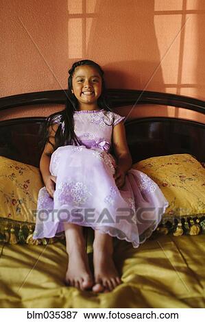 Stock Photo - Hispanic girl wearing party dress on bed. Fotosearch