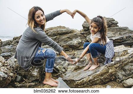 Stock Image - Hispanic mother and daughter making heart shape in tide pools. Fotosearch
