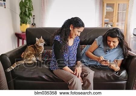 Stock Photo - Hispanic mother and daughter using cell phone on sofa. Fotosearch