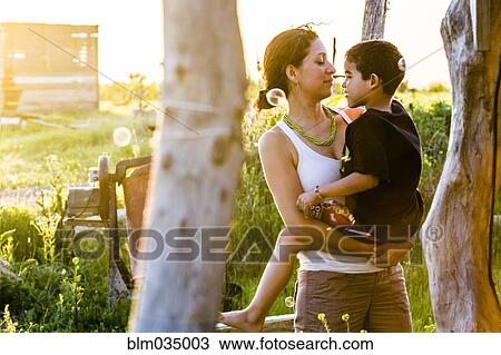 Stock Image - Hispanic mother carrying son in garden. Fotosearch