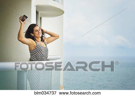 Stock Photo - Hispanic woman dancing near ocean on hotel balcony. Fotosearch