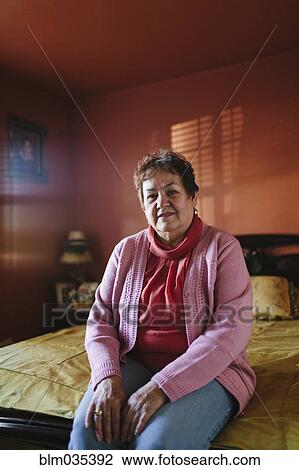 Stock Image - Hispanic woman sitting on bed. Fotosearch
