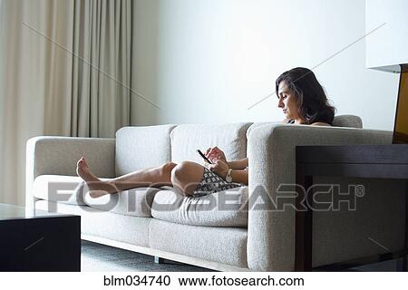 Stock Image - Hispanic woman using cell phone on hotel room sofa. Fotosearch