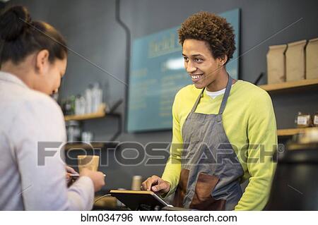 Stock Photograph - Mixed race barista assisting customer in coffee shop. Fotosearch