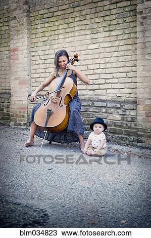 Stock Image - Mixed race musician playing cello with baby daughter. Fotosearch