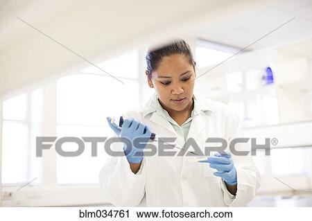 Stock Image - Mixed race scientist pipetting sample into tube in laboratory. Fotosearch