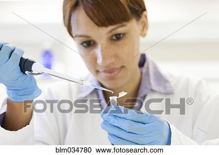 Stock Image - Mixed race scientist pipetting sample into test tube in laboratory. Fotosearch