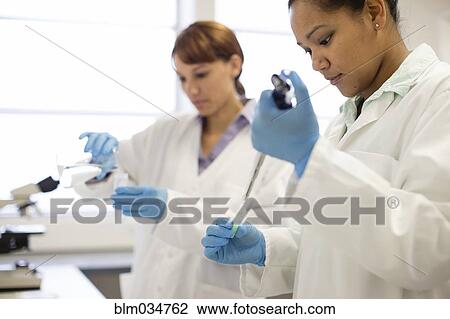 Stock Image - Mixed race scientists pipetting sample into tube in laboratory. Fotosearch