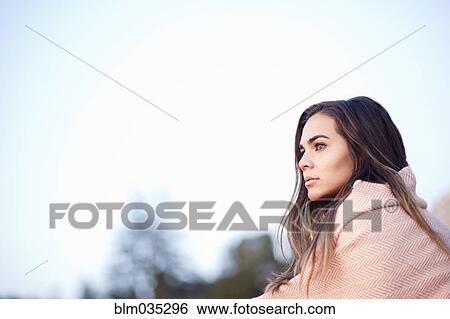 Stock Photograph - Mixed race woman wrapped in blanket under blue sky. Fotosearch