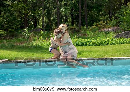 Stock Photo - Mother hugging son at swimming pool in backyard. Fotosearch