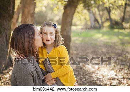 Stock Image - Mother kissing daughter in park. Fotosearch