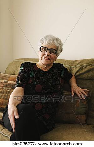 Stock Image - Older woman sitting on sofa. Fotosearch