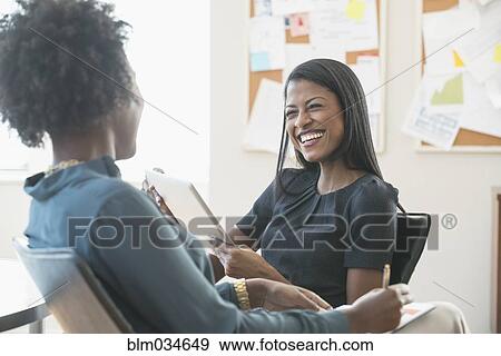 Stock Photo - Smiling businesswomen talking in office. Fotosearch