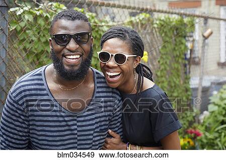 Stock Photo - Smiling couple wearing sunglasses near fence. Fotosearch
