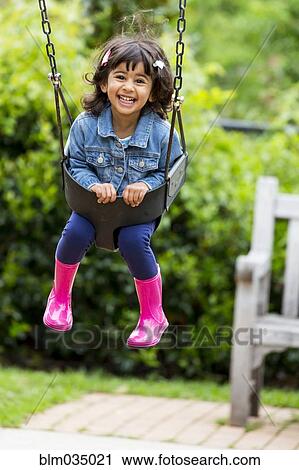 Stock Image - Smiling girl playing in swing at playground. Fotosearch