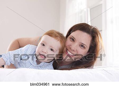 Stock Image - Smiling mother and son hugging on bed. Fotosearch