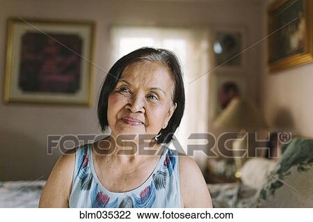 Stock Image - Smiling older woman sitting on bed. Fotosearch