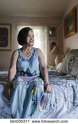 Stock Photo - Smiling older woman sitting on bed. Fotosearch
