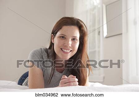 Stock Image - Smiling woman laying on bed. Fotosearch