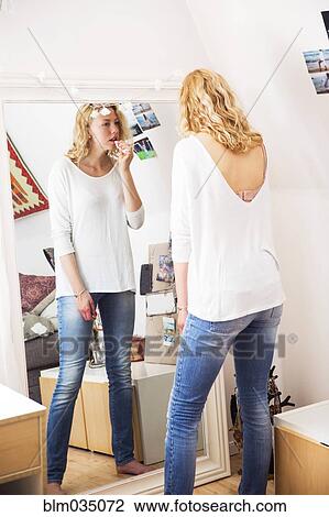 Stock Image - Woman applying lipstick in mirror. Fotosearch
